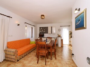 A dining area with a wooden table and chairs, a sofa, and a kitchen in the background.