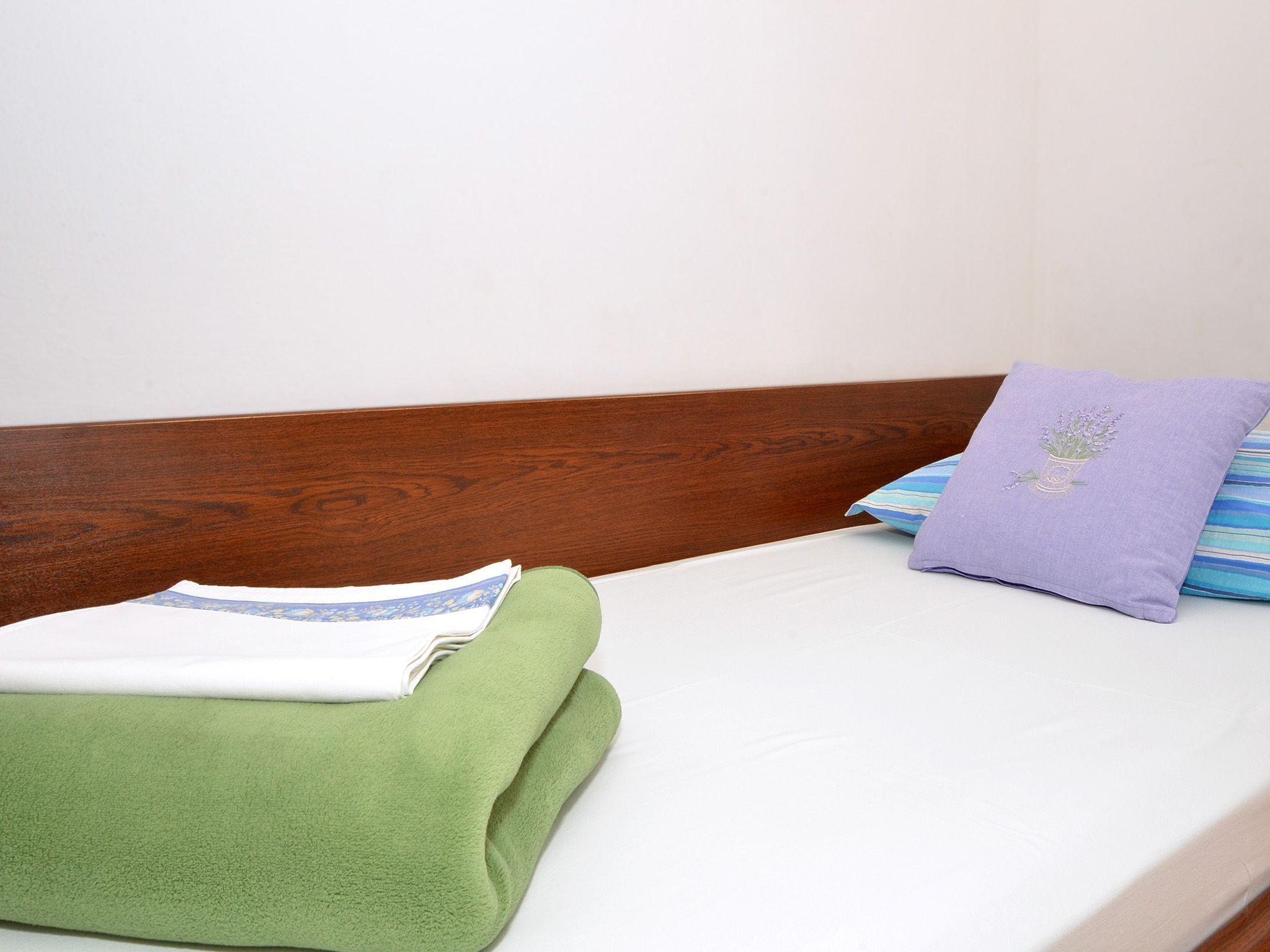 A bed with a wooden headboard, a green blanket, a purple pillow with a floral design, and a striped pillow.