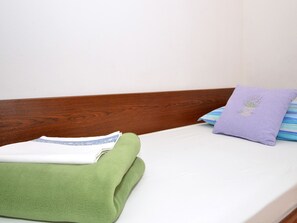 Uma cama com cabeceira de madeira, um cobertor verde e duas almofadas, uma delas com desenho floral.
