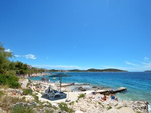Una playa con terreno rocoso, agua azul cristalina y algunas personas.