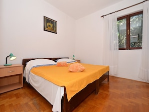 Un dormitorio con una cama de madera, una mesita de noche con lámpara, un cuadro en la pared y una ventana con cortinas.