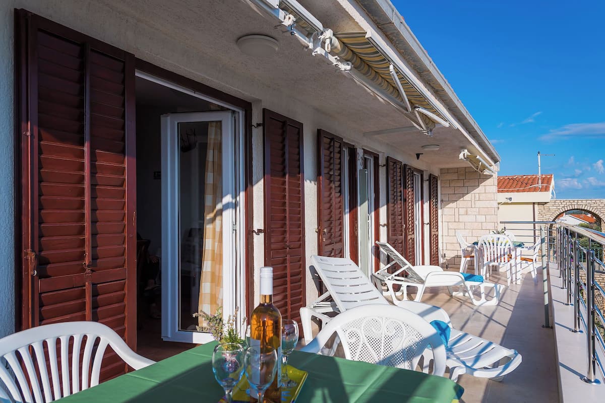 A balcony with white plastic chairs and a table, a bottle of wine, and a view of the sea.
