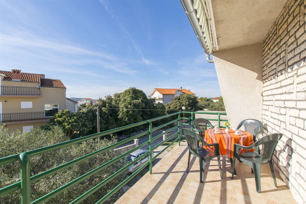 Ein Balkon mit Tisch und Stühlen, einem grünen Geländer und Blick auf die Straße und Häuser.