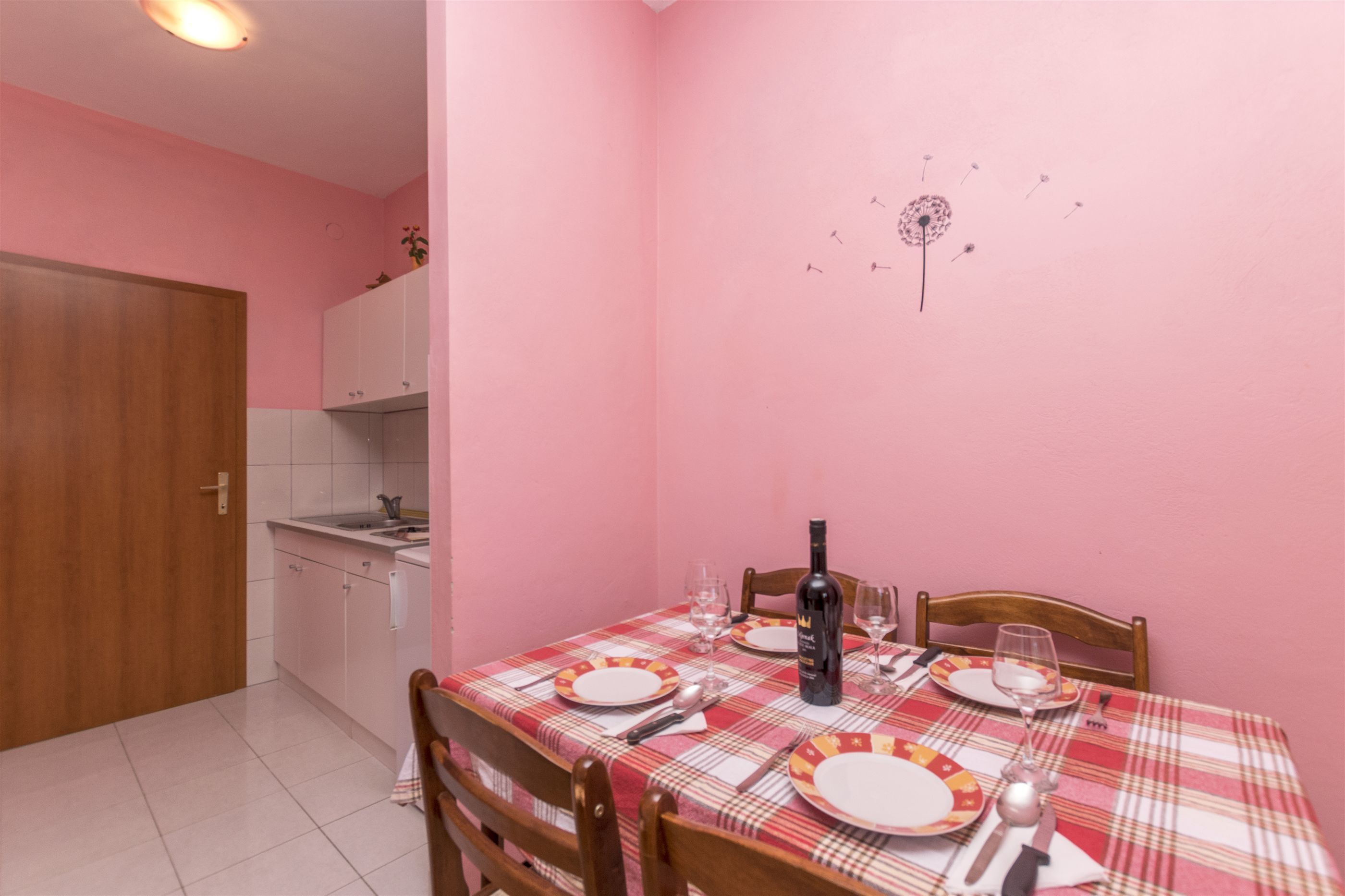 Comedor con una mesa dispuesta para cuatro personas, una botella de vino y un adorno en la pared.
