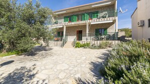 Un edificio a due piani con facciata in pietra, persiane verdi e un balcone con ringhiera in metallo.