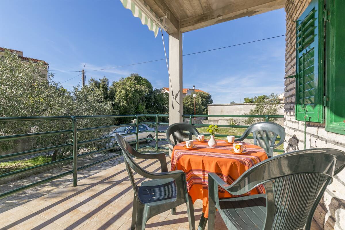 Eine Terrasse mit Tisch für zwei Personen, Gartenstühlen und Blick auf eine Straße mit parkenden Autos.