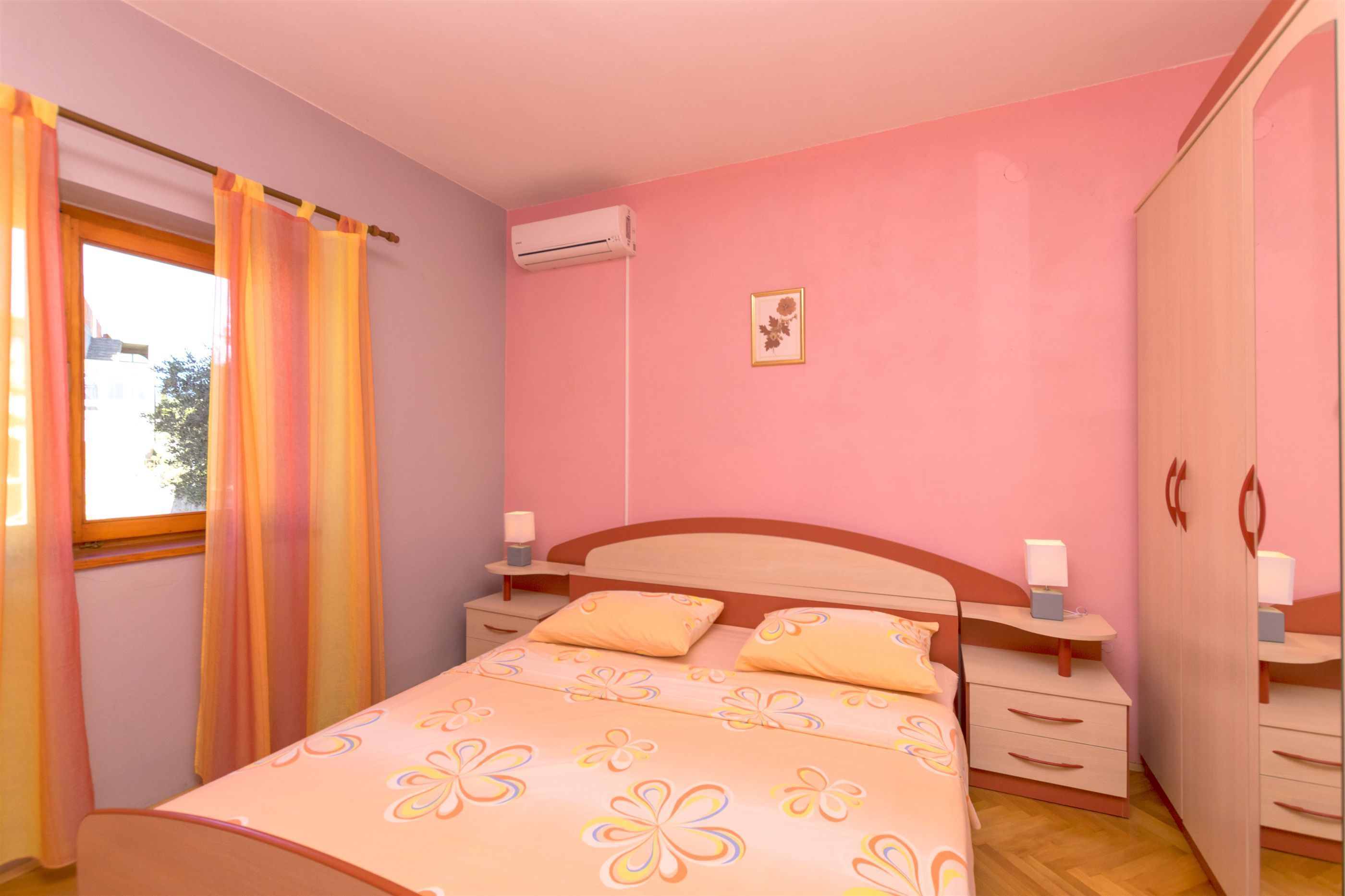 Een slaapkamer met een bed, nachtkastjes, een airconditioning, een kledingkast en een raam met gordijnen.