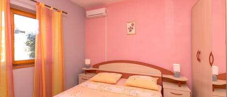 A bedroom with a bed, bedside tables, an air conditioning unit, a wardrobe, and a window with curtains.