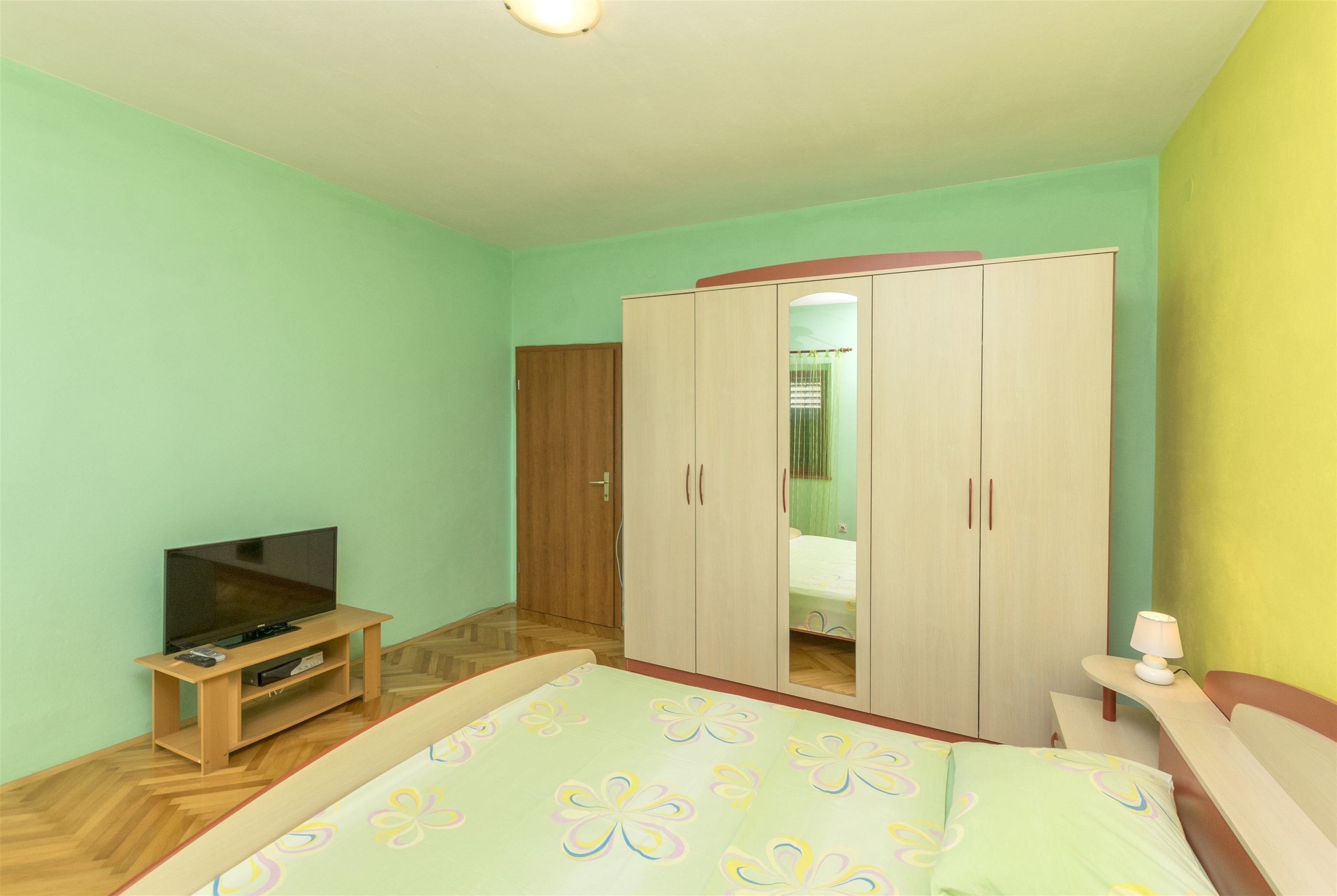 Ein Schlafzimmer mit Bett, Schrank, Fernseher auf einem Tisch und Nachttisch mit Lampe.