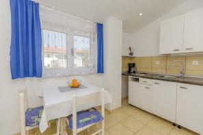 A small kitchen with white cabinets, a sink, and a window with blue curtains. - Apartments and Rooms On the Beach (Vodice)