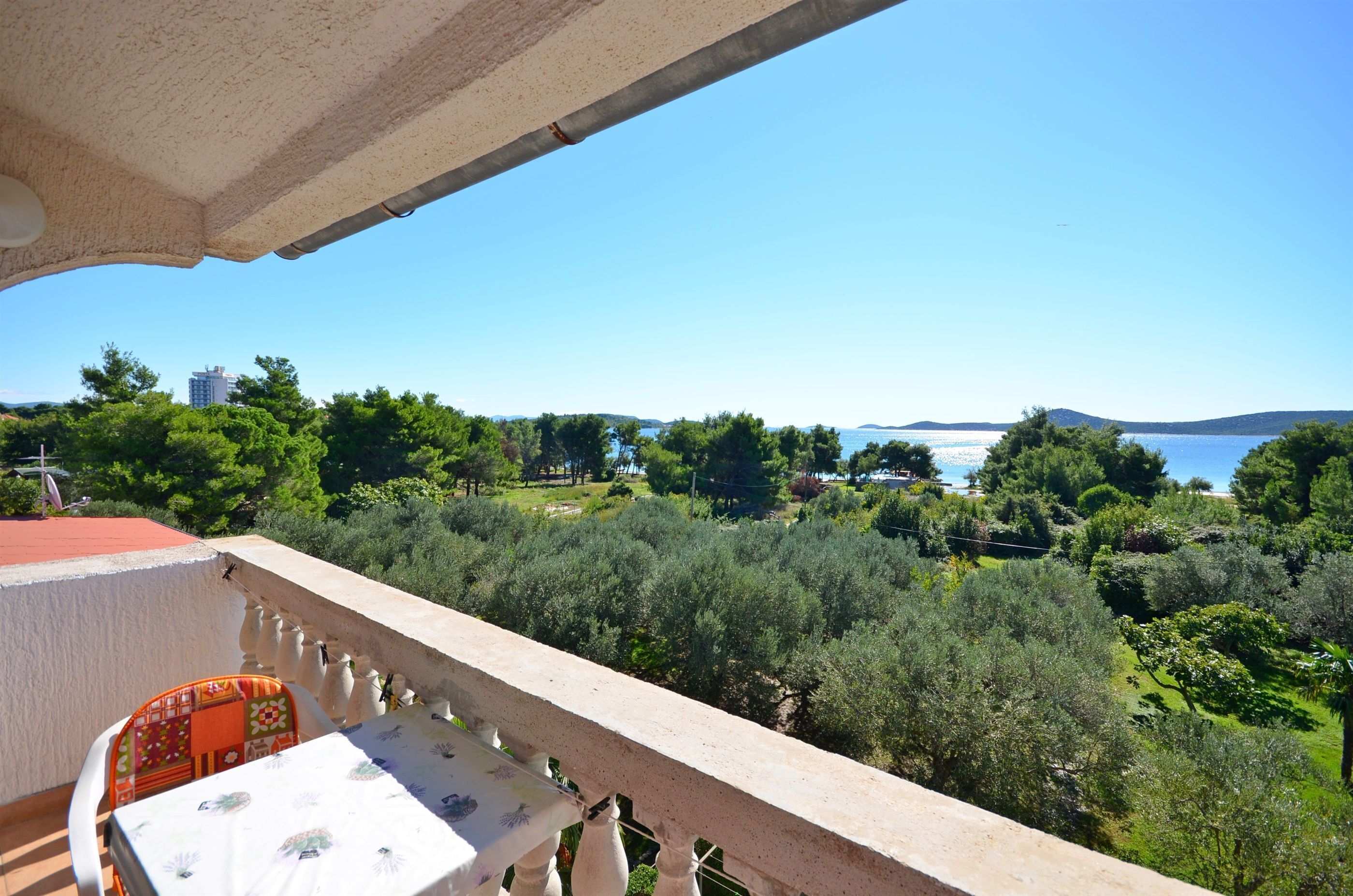 A balcony with a table and chairs, overlooking a lush green landscape and a body of water.