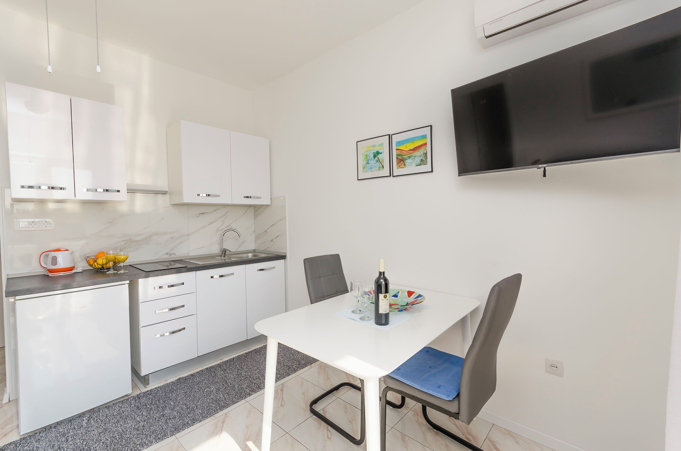 A modern kitchen with white cabinets, a built-in oven, and a dining area with a white table and chairs.