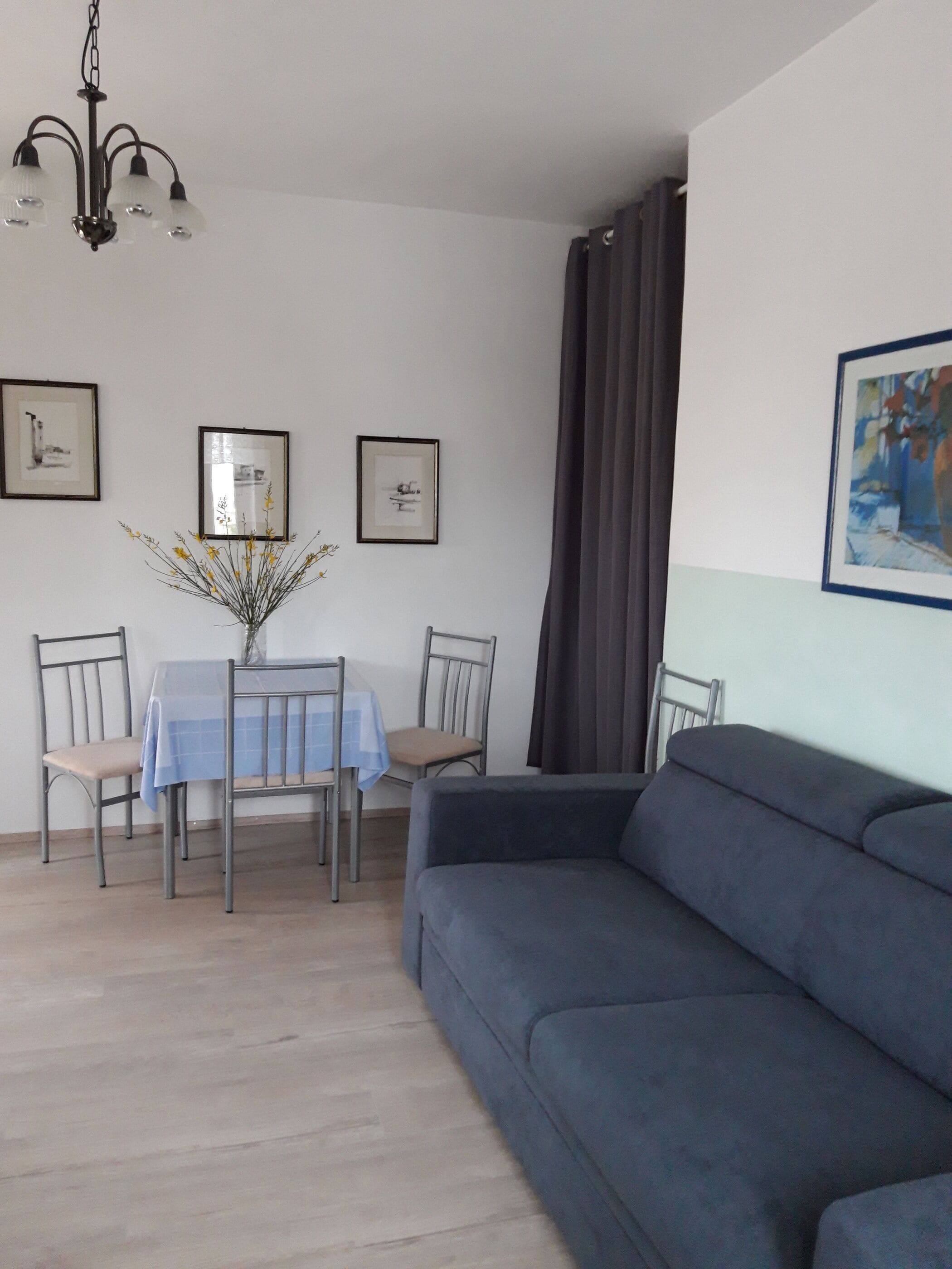En stue med en blå sofa, et spisebord med stole, en lysekrone og billeder i rammer på væggene.