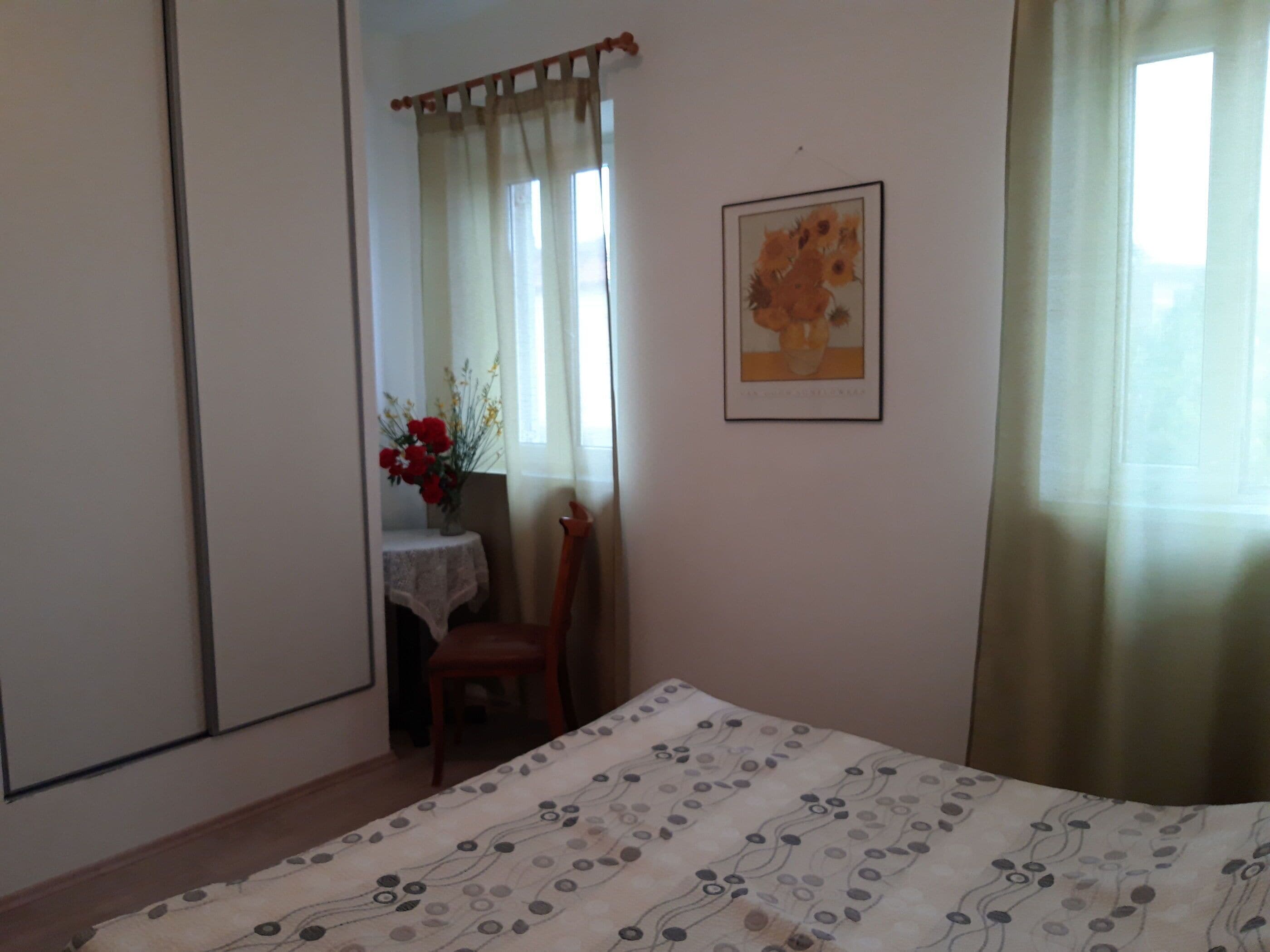 A bedroom with a bed, a chair, a table with a vase of flowers, and a framed picture on the wall.
