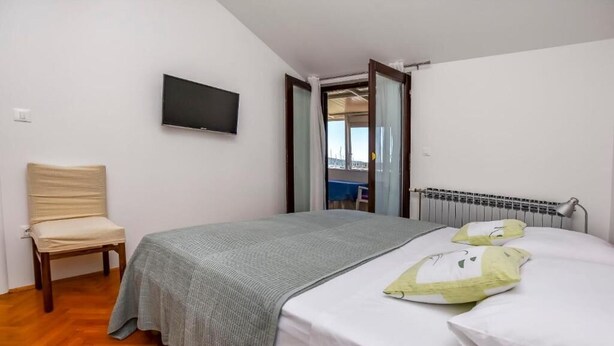 A bedroom with a bed, a chair, a TV, and a view of the outside. - Apartments Sime (Rogoznica)