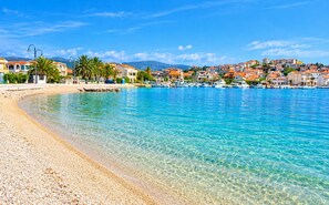 A coastal town with clear blue waters, a pebble beach, and buildings with red roofs. - Apartments Sime (Rogoznica)