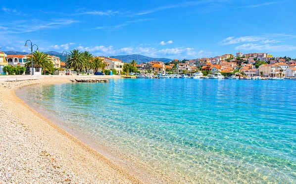 A coastal town with clear blue waters, a pebble beach, and buildings with red roofs. - Apartments Sime (Rogoznica)