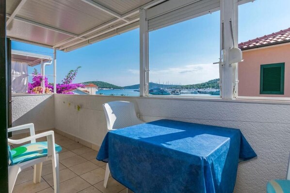 A balcony with a table and chair, a view of the sea, and a building with a red roof. - Apartments Sime (Rogoznica)