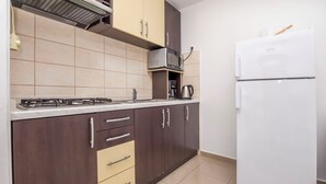 A kitchen with dark brown cabinets, a white refrigerator, a microwave, and a gas stove. - Apartments Antea (Rogoznica)