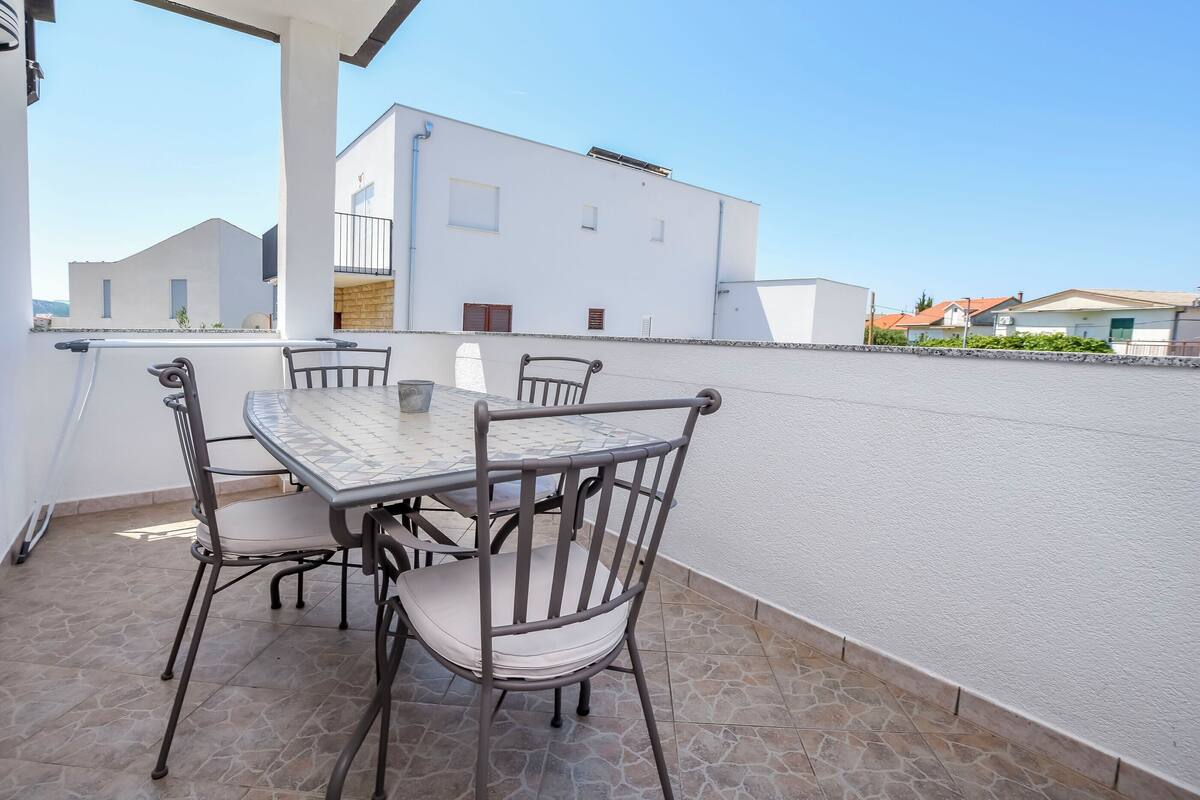 Une terrasse sur le toit avec une table et des chaises, un bâtiment blanc en arrière-plan et un ciel dégagé.