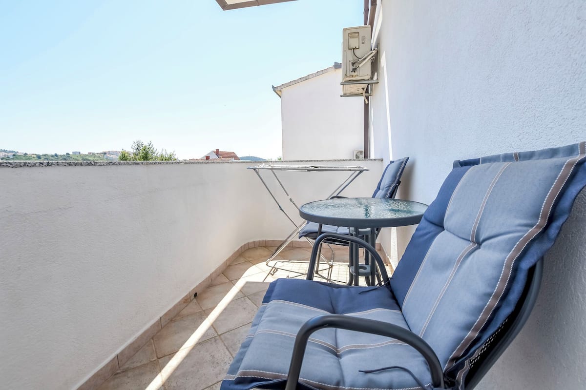 Un balcon avec une chaise bleue dotée d’un coussin, une petite table ronde et une chaise en métal.