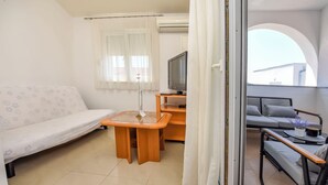 A modern, well-lit room with a sofa, a small wooden table, a TV, and a balcony with a sofa and a table. - Apartments Antea (Rogoznica)