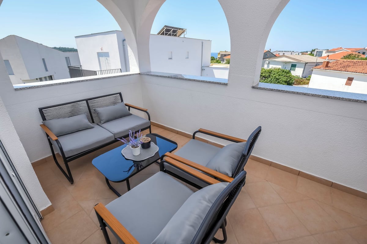 Une terrasse sur le toit, aménagée avec un espace salon comprenant un canapé et des fauteuils, une petite table agrémentée d’un objet décoratif, et offrant une vue sur les bâtiments environnants.