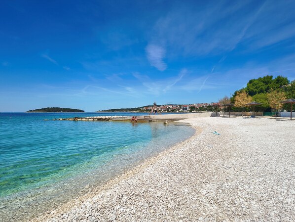 A pebble beach with clear water, a wooden swing, and a distant town.