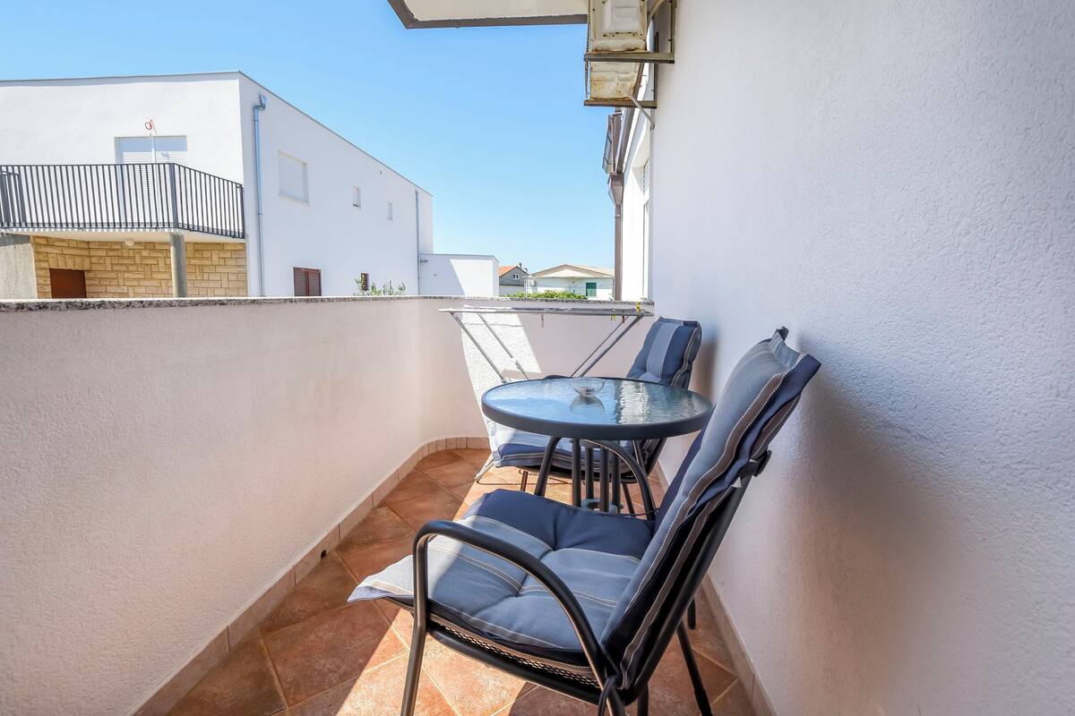 Un petit balcon extérieur avec une table ronde en verre et deux chaises.