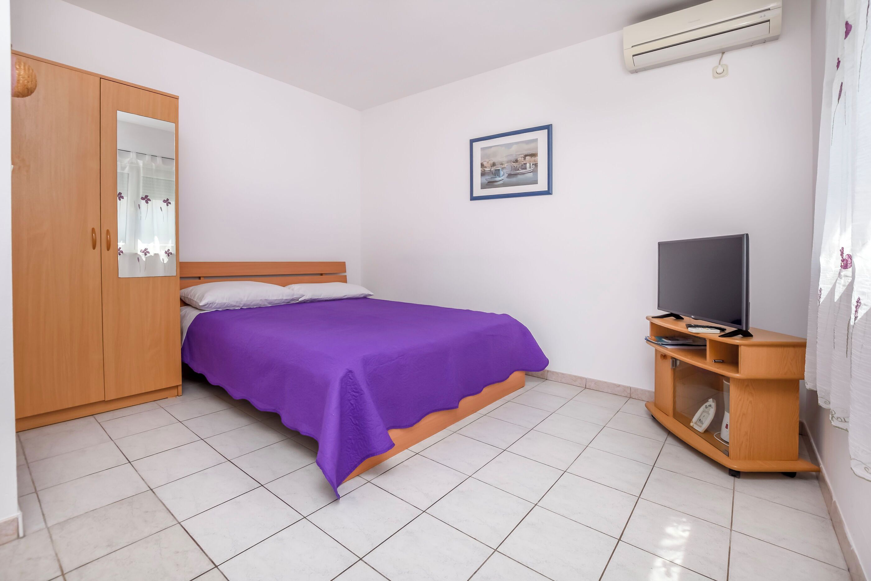 Une chambre à coucher comprenant un lit, une armoire, un meuble pour la télévision et un appareil de climatisation.