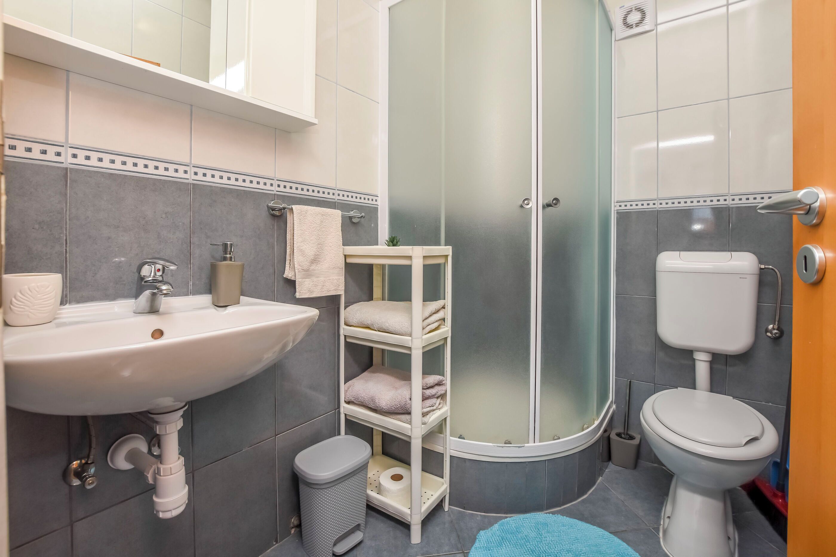 Egy modern fürőszoba mosdókagylóval, WC-vel és üvegfalas zuhanyzóval.