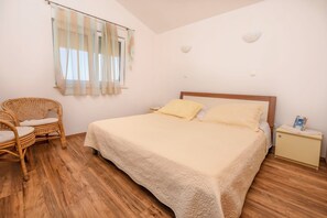 A bedroom with a bed, a nightstand, a chair, and a window with sheer curtains. - Apartments Antea (Rogoznica)