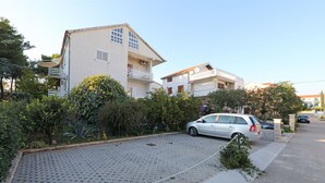 Zona residencial con entrada pavimentada, coches aparcados y casas con balcones.