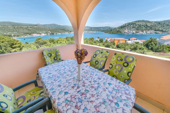 Un balcon avec une table et des chaises, un vase rempli de fleurs et une vue panoramique sur un lac et des collines.