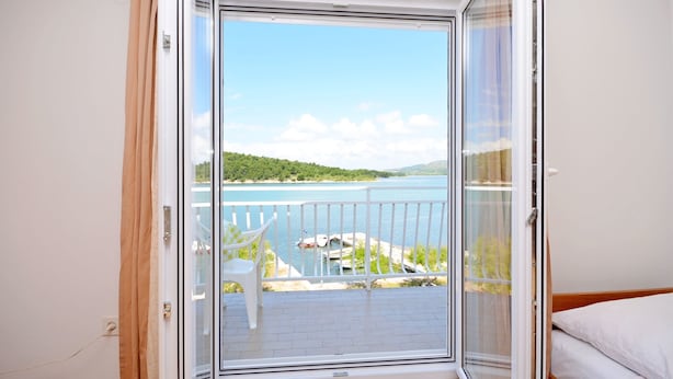 A room with a sliding glass door leading to a balcony with a view of a lake and greenery. - Apartments Vila Punta (Jadrtovac)