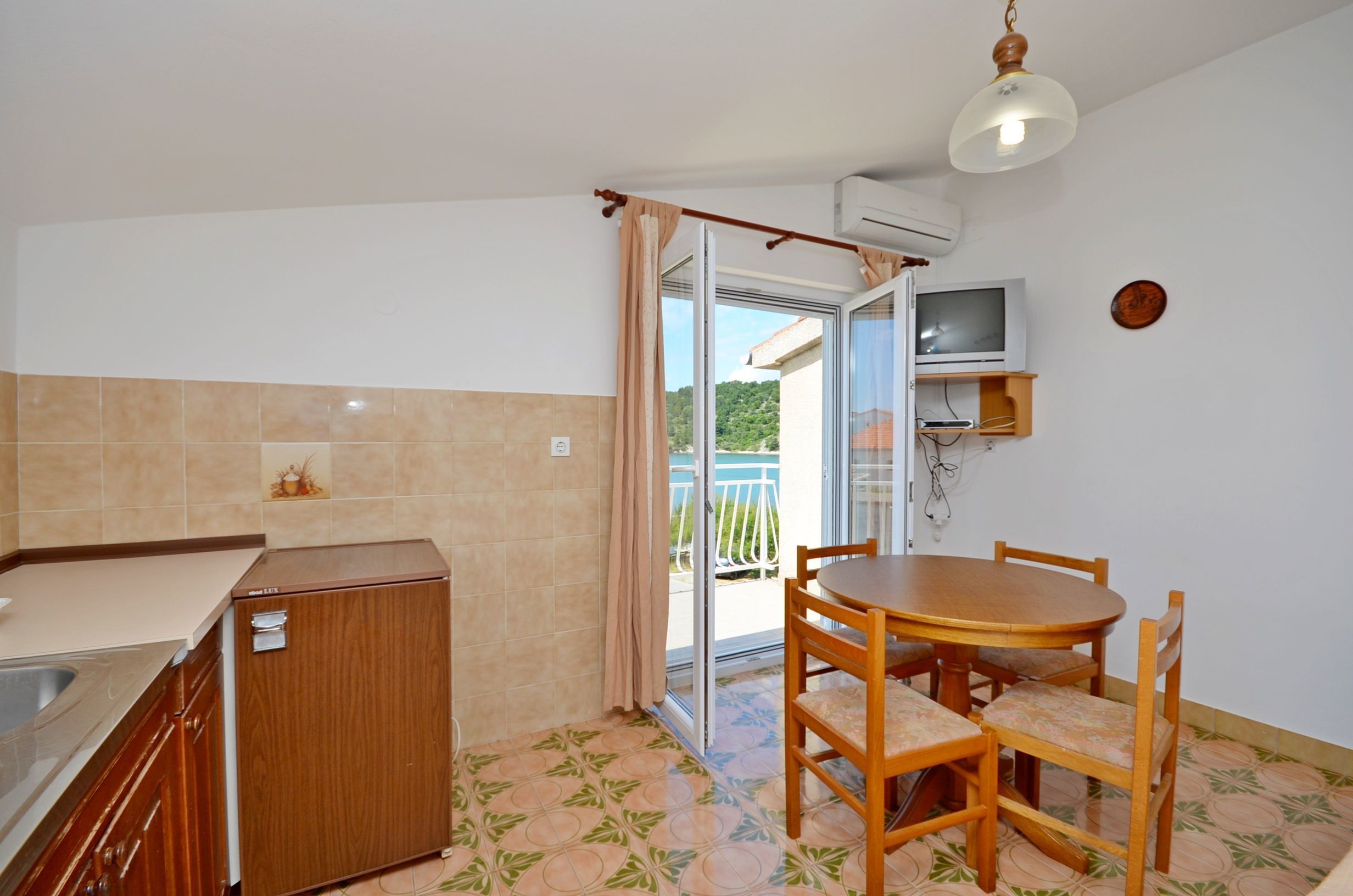 Una cocina compacta con estufa integrada, un refrigerador pequeño y un comedor con una mesa redonda y sillas.