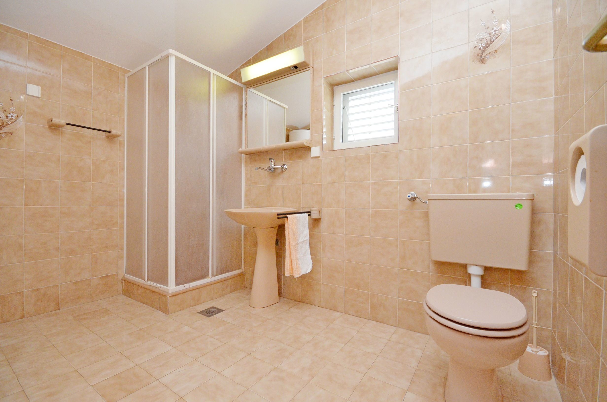 Une salle de bain avec une douche, un lavabo, des toilettes et une petite fenêtre.