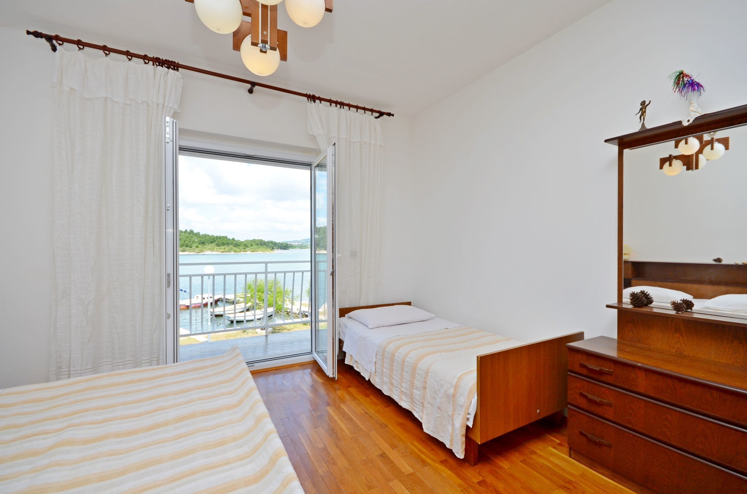 Un dormitorio con cama, cómoda y vista a un balcón con barandilla y un cuerpo de agua.