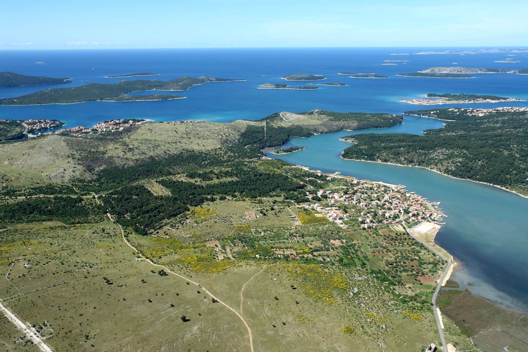 Vista aérea de uma cidade costeira, com um rio serpenteando por ela, cercada por colinas verdes e o mar.