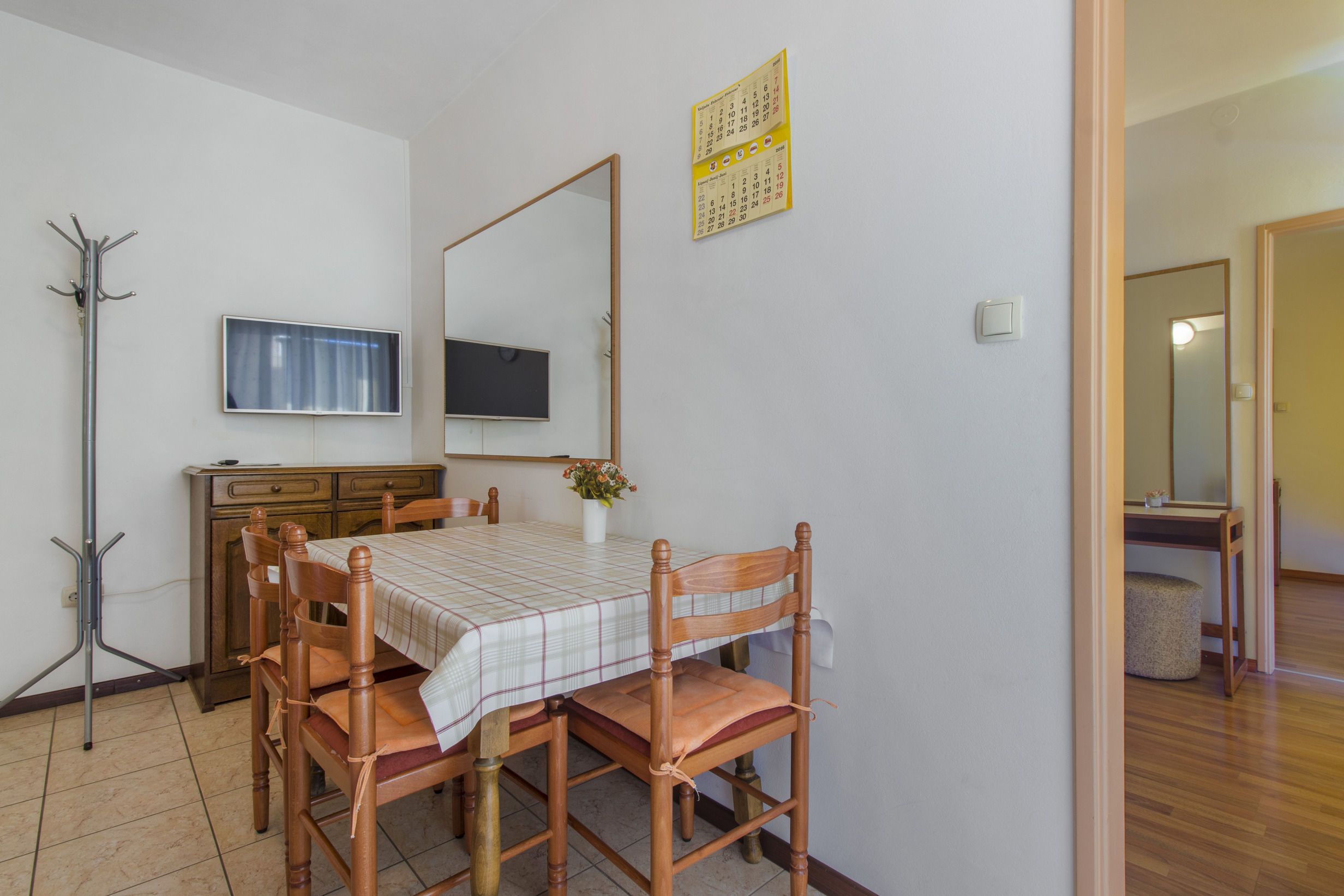 A dining area with a table, chairs, a coat rack, a flat-screen TV, and a calendar on the wall.