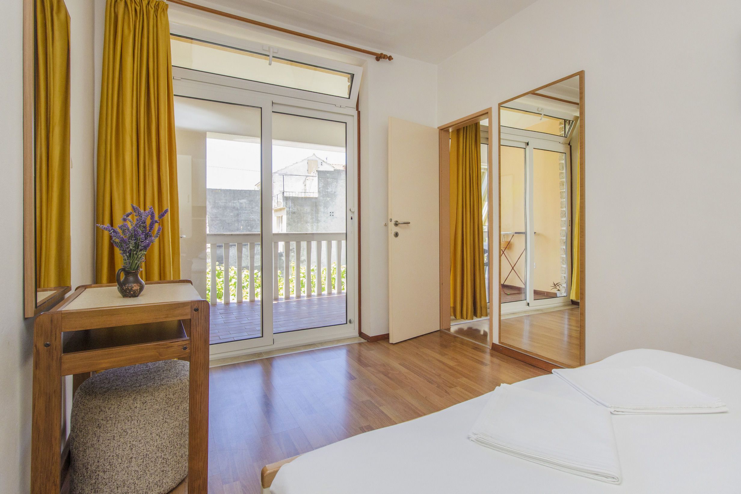 Une chambre d’hôtel comprenant un lit, un bureau avec une chaise, une petite table avec un vase et une porte-fenêtre coulissante donnant sur un balcon.