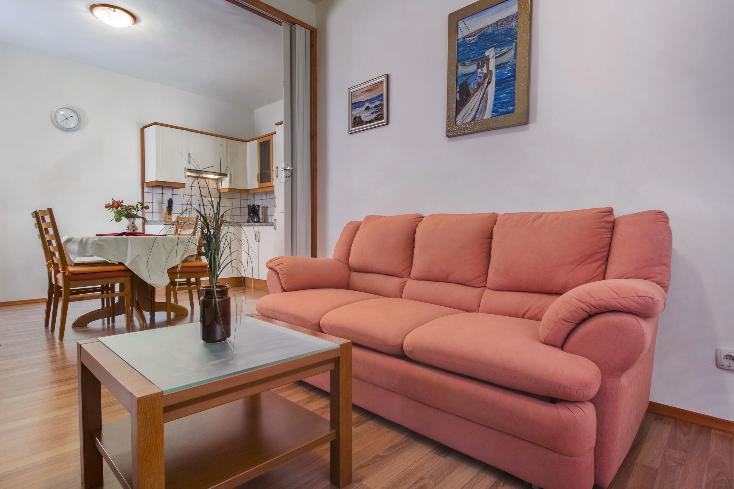 A living room with a sofa, a dining table with chairs, a coffee table, and a kitchen area in the background.