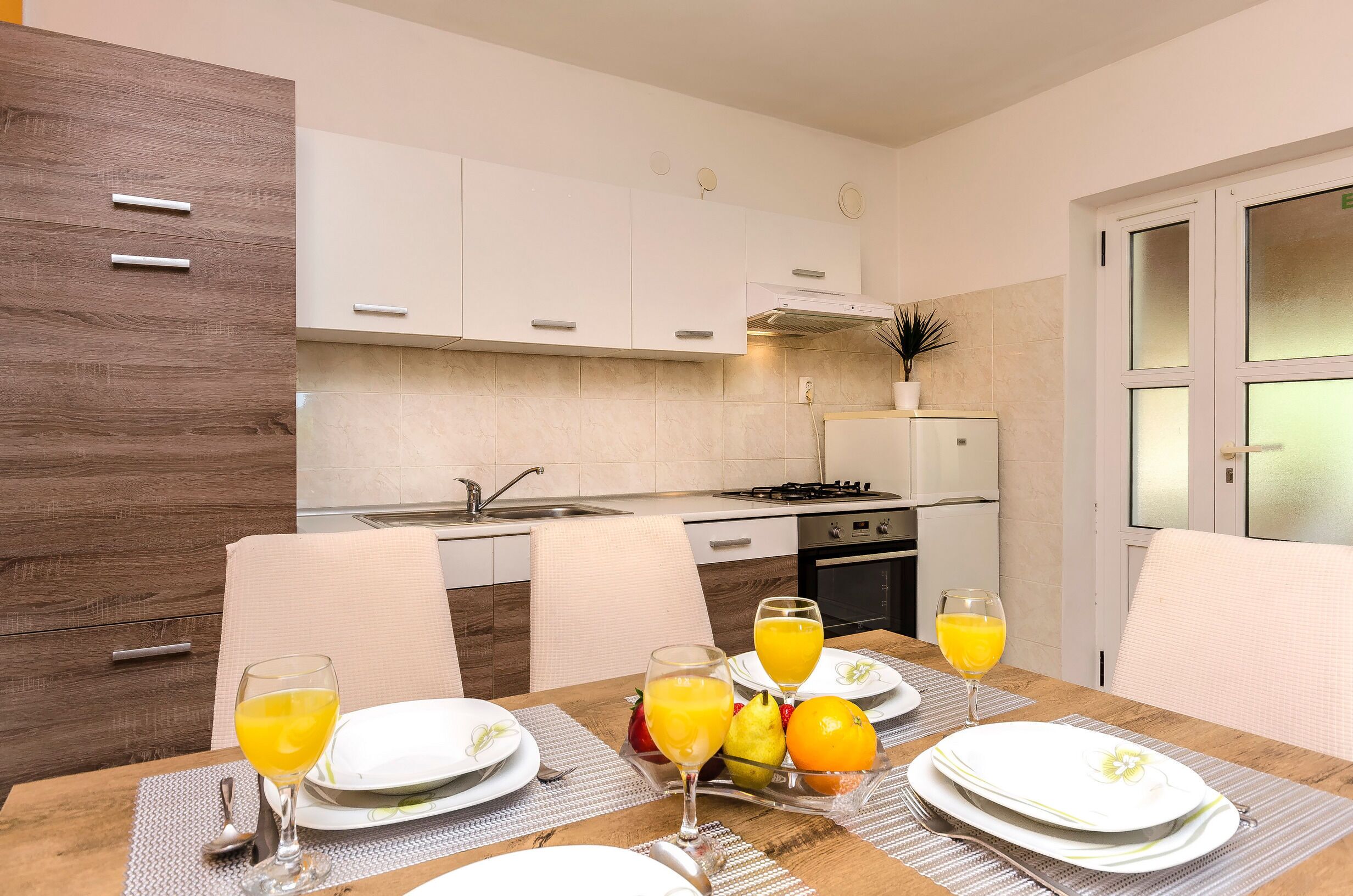 A modern kitchen with white cabinets, a dining table set with plates, glasses, and fruit.