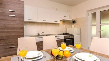 A modern kitchen with white cabinets, a dining table set with plates, glasses, and fruit.