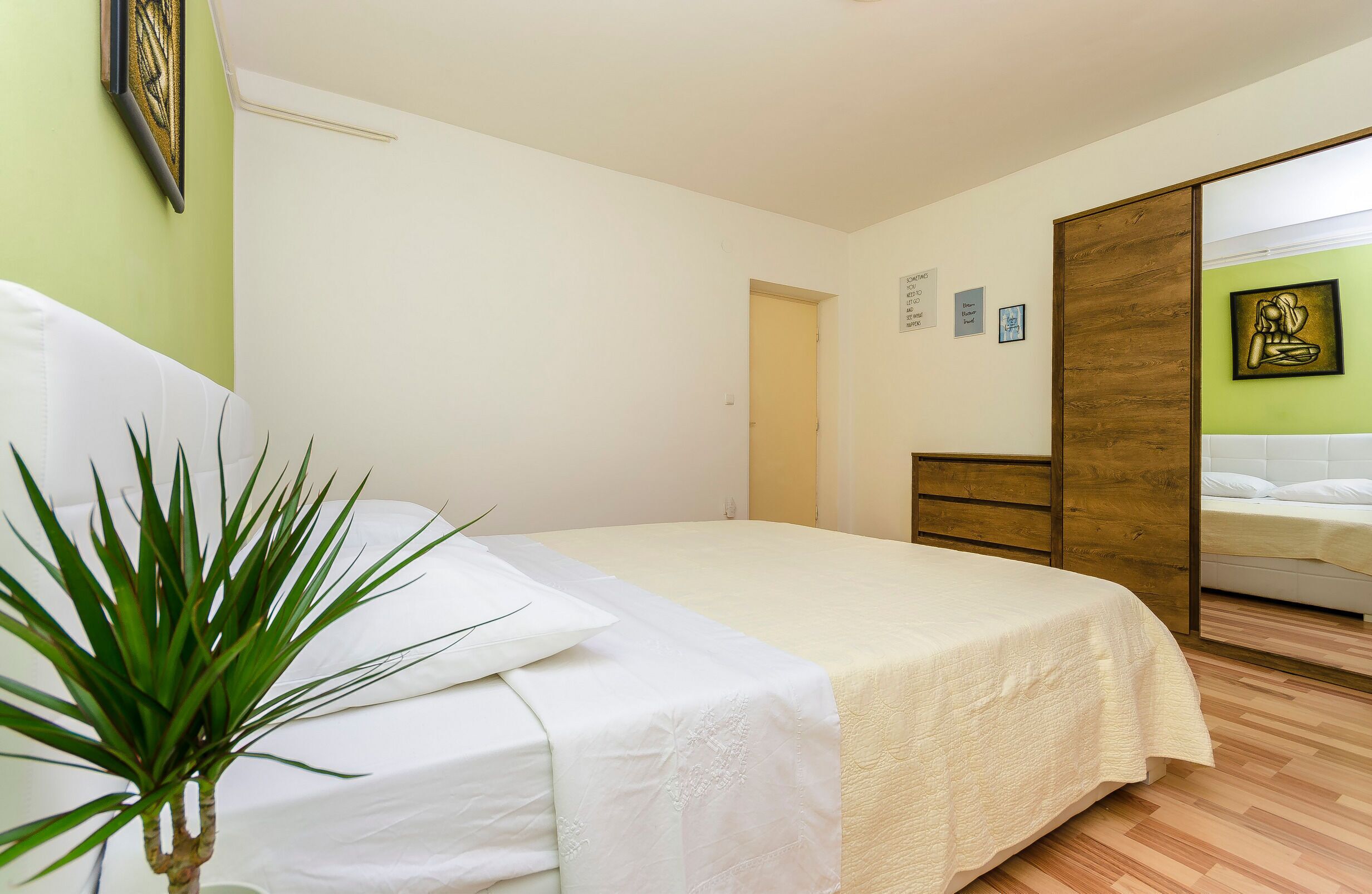 Un dormitorio con una cama, una planta en la mesita de noche, un armario de madera y una pared verde.