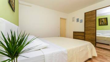 Un dormitorio con una cama, una planta en la mesita de noche, un armario de madera y una pared verde.