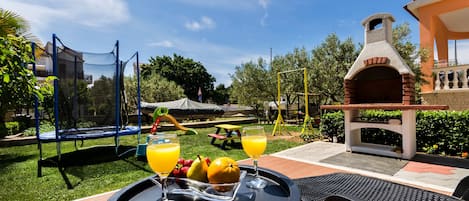 An outdoor patio with a table set for breakfast, a trampoline, and a brick oven.
