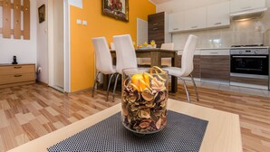 Una cocina moderna con armarios blancos, un comedor con mesa y sillas, y un jarrón de vidrio decorativo con flores secas sobre una mesa.