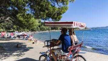 A beach scene with a red and white striped canopy, people relaxing on the sand, and a body of water in the background.
