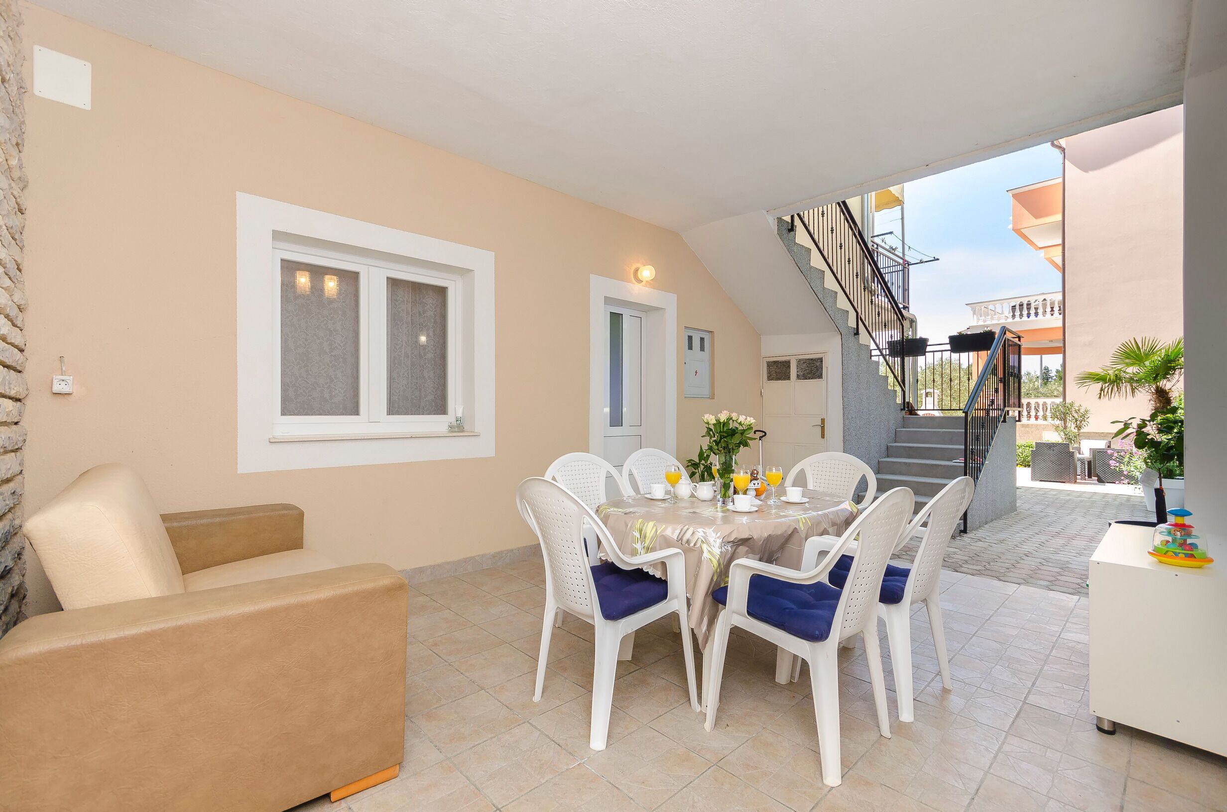 Un coin repas avec une table dressée pour quatre personnes, entourée de chaises blanches dotées de coussins bleus. Un canapé beige est placé sur le côté gauche.
